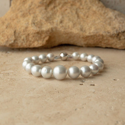 An Australian South Sea pearl strand bracelet with a 9ct white gold clasp, displayed on a textured beige stone surface with a larger rock in the background.