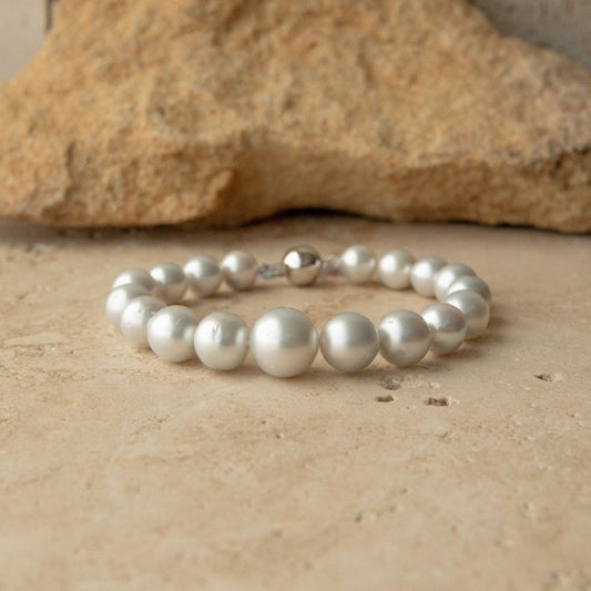 An Australian South Sea pearl strand bracelet with a 9ct white gold clasp, displayed on a textured beige stone surface with a larger rock in the background.