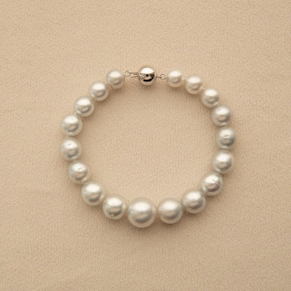 A strand bracelet made of silver Australian South Sea pearls with a polished 9ct white gold clasp, displayed on a textured beige background.