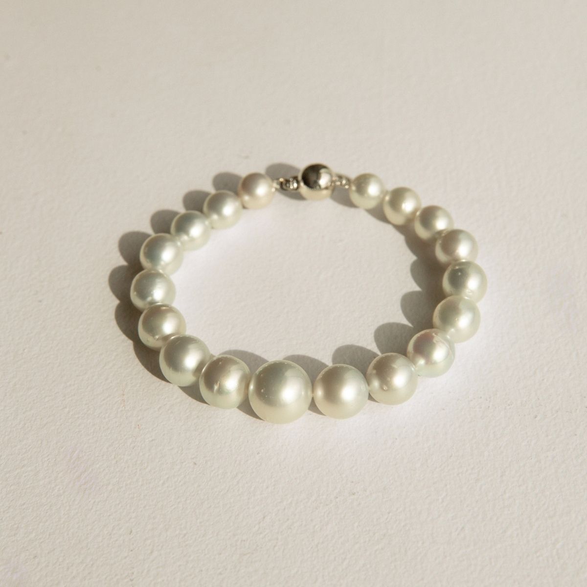 A graduated pearl strand bracelet with a polished 9ct white gold clasp, displayed on a textured off-white surface.