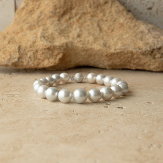 A strand bracelet made of lustrous white Australian South Sea pearls arranged in a circle, resting on a textured beige stone surface with a larger tan rock in the blurred background.