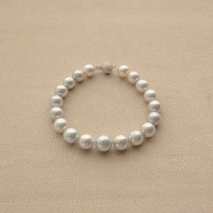 A strand bracelet made of white, round Australian South Sea pearls with a small 9ct white gold clasp, displayed on a textured beige surface.