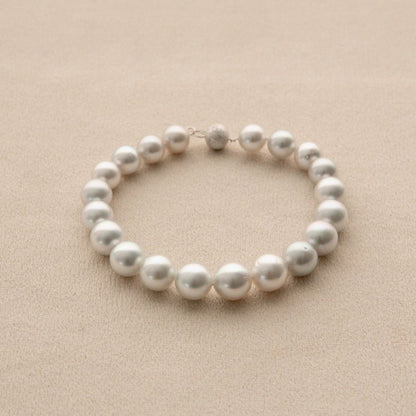 A strand bracelet made of white Australian South Sea pearls arranged in a circle on a textured beige background.
