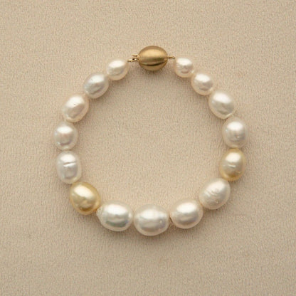 A Semi Drop pearl strand bracelet with a gold clasp, displayed on a textured beige background.