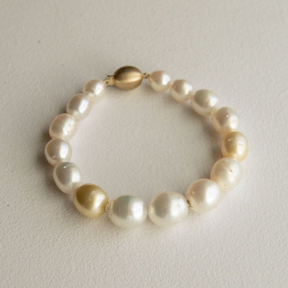A pearl strand bracelet made of semi drop Cygnet Bay grown Australian South Sea pearls with a polished gold clasp, displayed on a textured off-white surface.