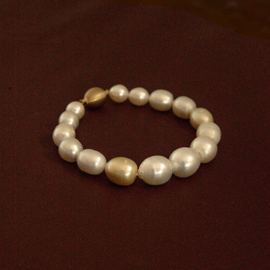 A strand bracelet made of multicolour Australian South Sea pearls with two larger champagne-gold beads, displayed on a dark reddish-brown background.