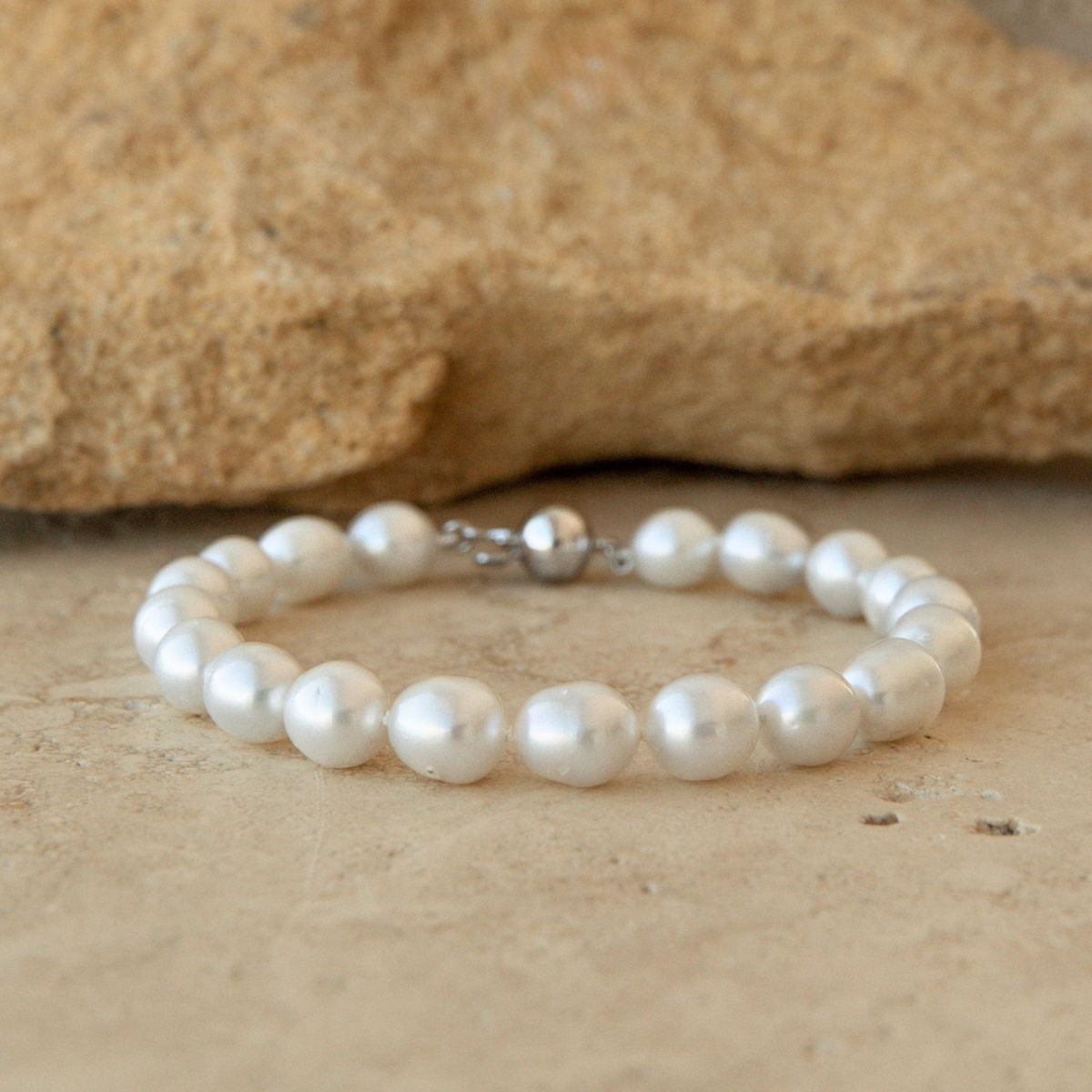 Pearl strand bracelet on a sandy surface with a rock in the background