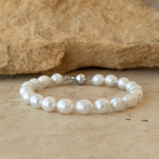 Pearl strand bracelet on a sandy surface with a rock in the background