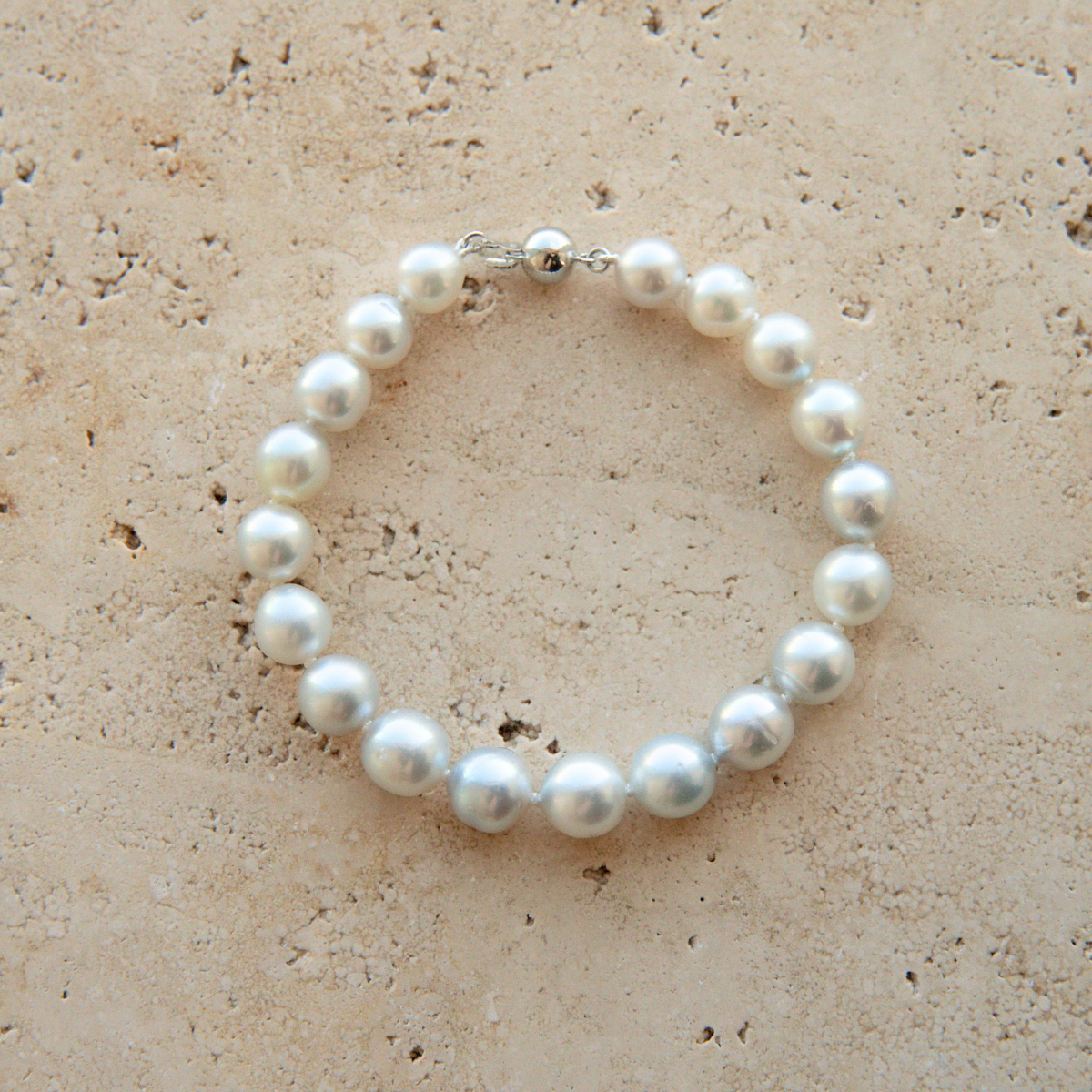 A pearl strand bracelet with a silver-toned clasp, displayed on a textured beige stone surface.