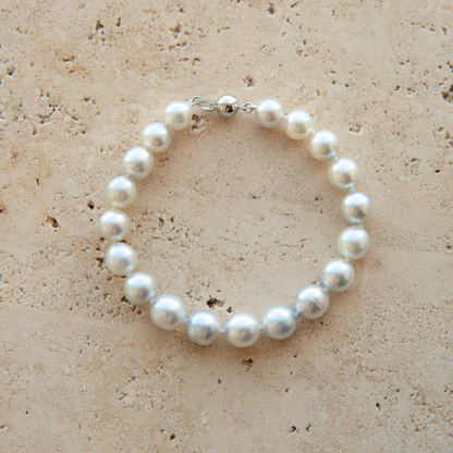 A pearl strand bracelet with a silver-toned clasp, displayed on a textured beige stone surface.