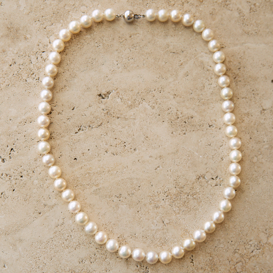Pearl strand necklace on a textured beige surface