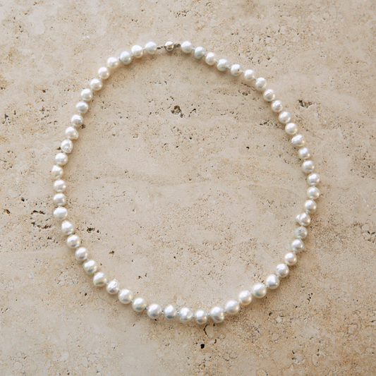 Pearl strand necklace on a textured beige surface