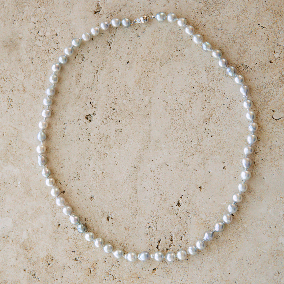 Pearl strand necklace on a beige stone surface