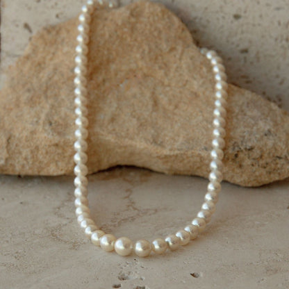 A strand of cream toned Australian Akoya pearls draped over a natural beige stone on a textured stone surface.