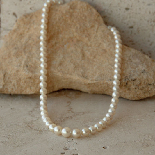 A strand of cream toned Australian Akoya pearls draped over a natural beige stone on a textured stone surface.