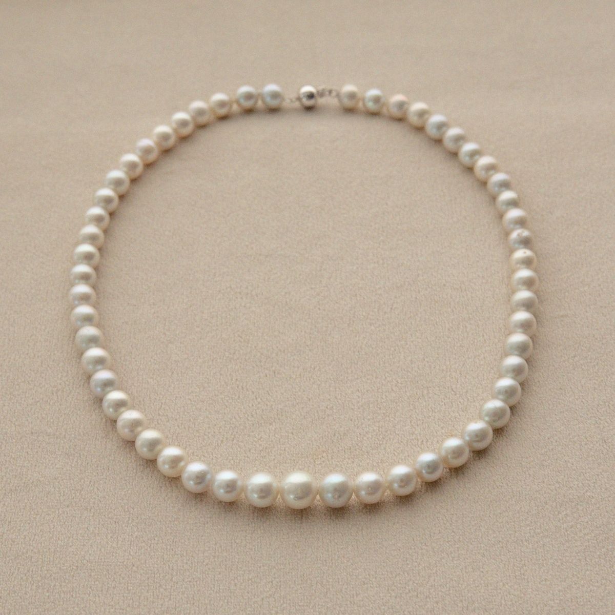 A single-strand Australian Akoya pearl strand necklace with round, off-white pearls and a silver clasp, displayed on a textured beige surface.