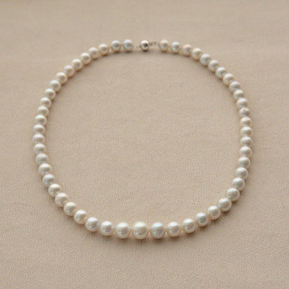 A single-strand Australian Akoya pearl strand necklace with round, off-white pearls and a silver clasp, displayed on a textured beige surface.