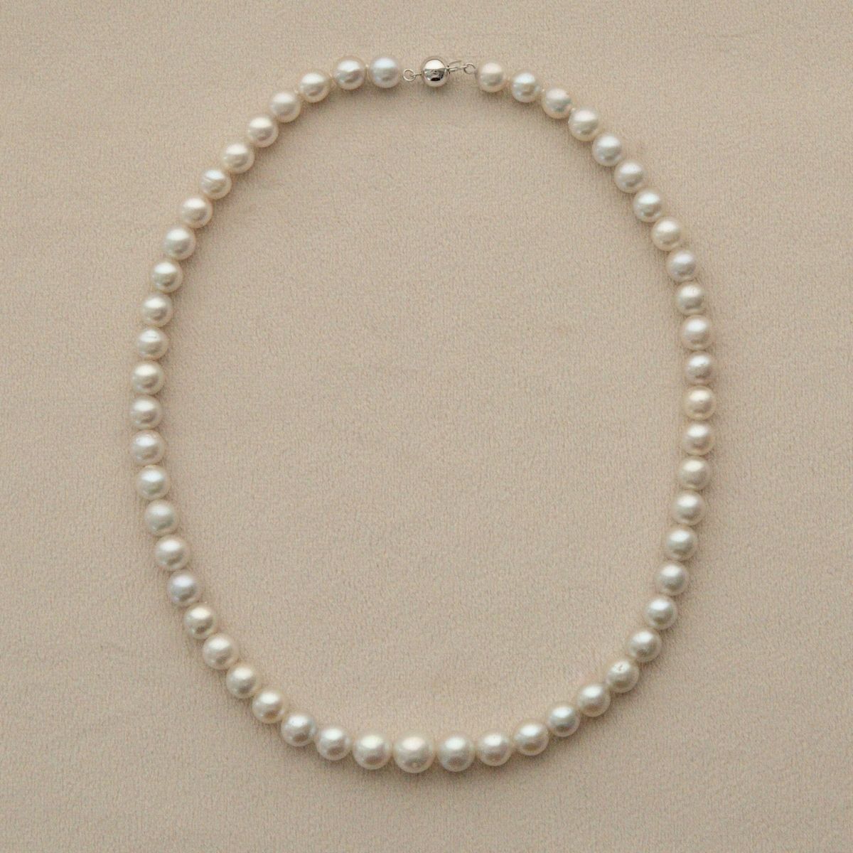 A classic, graduated Australian Akoya pearl strand necklace with a 9ct white gold clasp, arranged in a neat circle on a textured beige background.