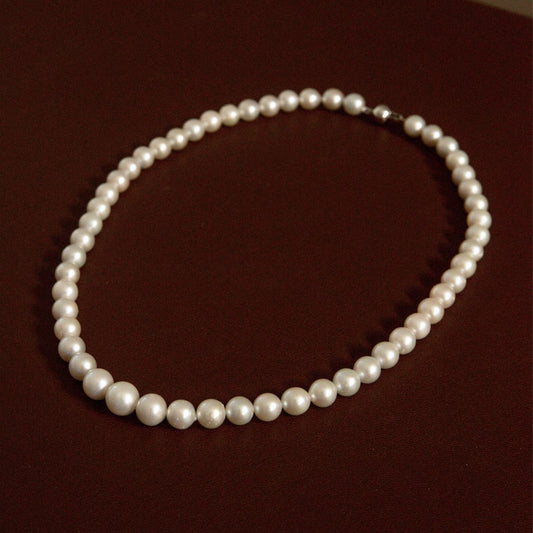 A classic single-strand Australian Akoya pearl strand necklace with lustrous white pearls and a 9ct white gold clasp, displayed on a dark brown background.