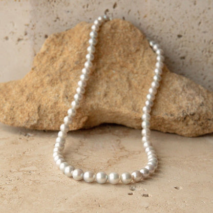 A white Australian Akoya pearl strand necklace draped over a natural tan rock on a textured beige stone surface.