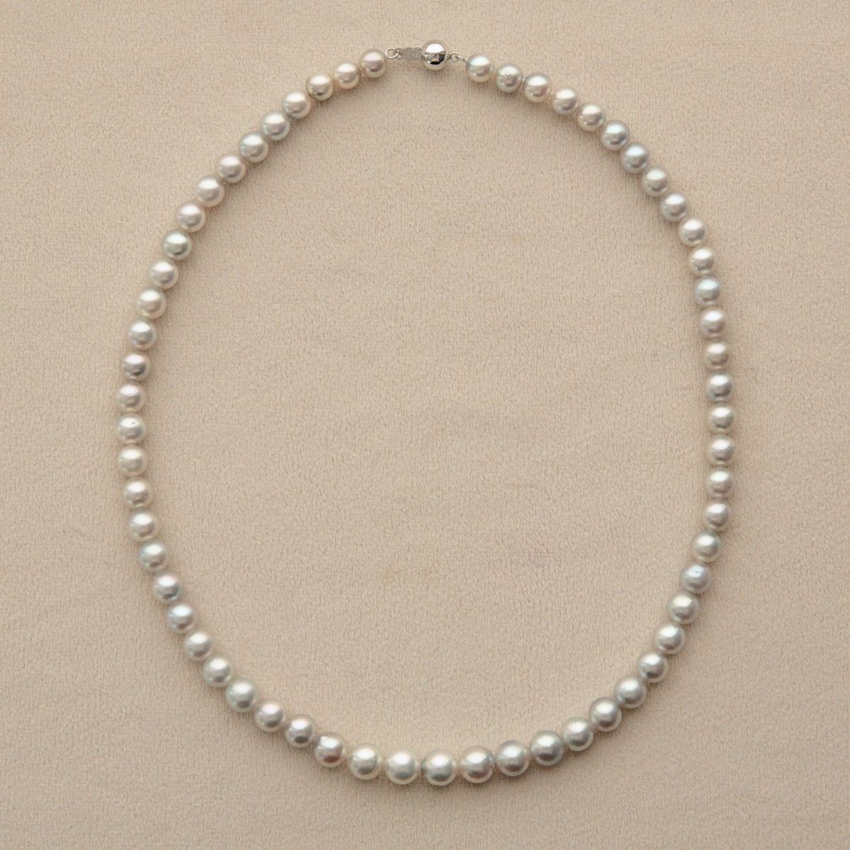 A classic Australian pearl strand necklace with uniform white pearls and a 9ct white gold clasp, displayed on a neutral beige textured background.