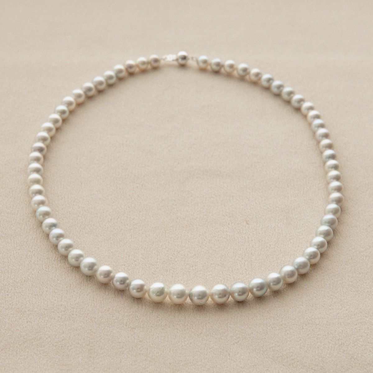 A classic Australian Akoya pearl strand necklace with round, lustrous white pearls on a light beige textured background.