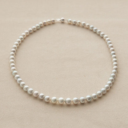 A classic Australian Akoya pearl strand necklace with round, lustrous white pearls on a light beige textured background.