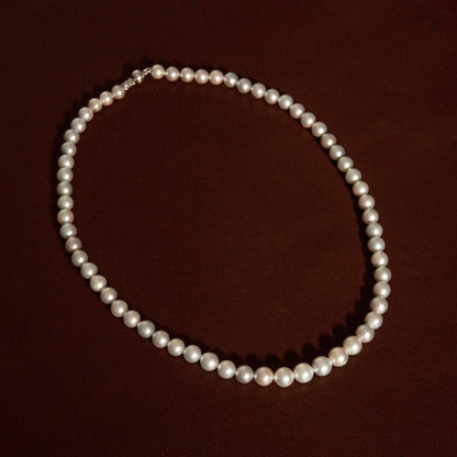 A classic single-strand pearl strand necklace with a 9ct white gold clasp, displayed on a dark brown background.