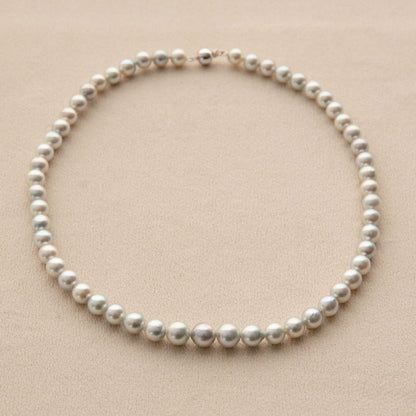 A single-strand pearl necklace with round, lustrous silver Akoya pearls and a small 9ct white gold clasp, displayed on a textured beige background.