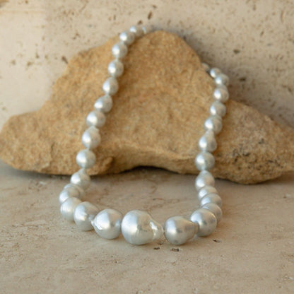 A strand necklace of irregular baroque Australian South Sea pearls draped over a tan stone on a textured beige surface.