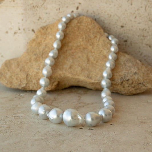 A strand necklace of irregular baroque Australian South Sea pearls draped over a tan stone on a textured beige surface.