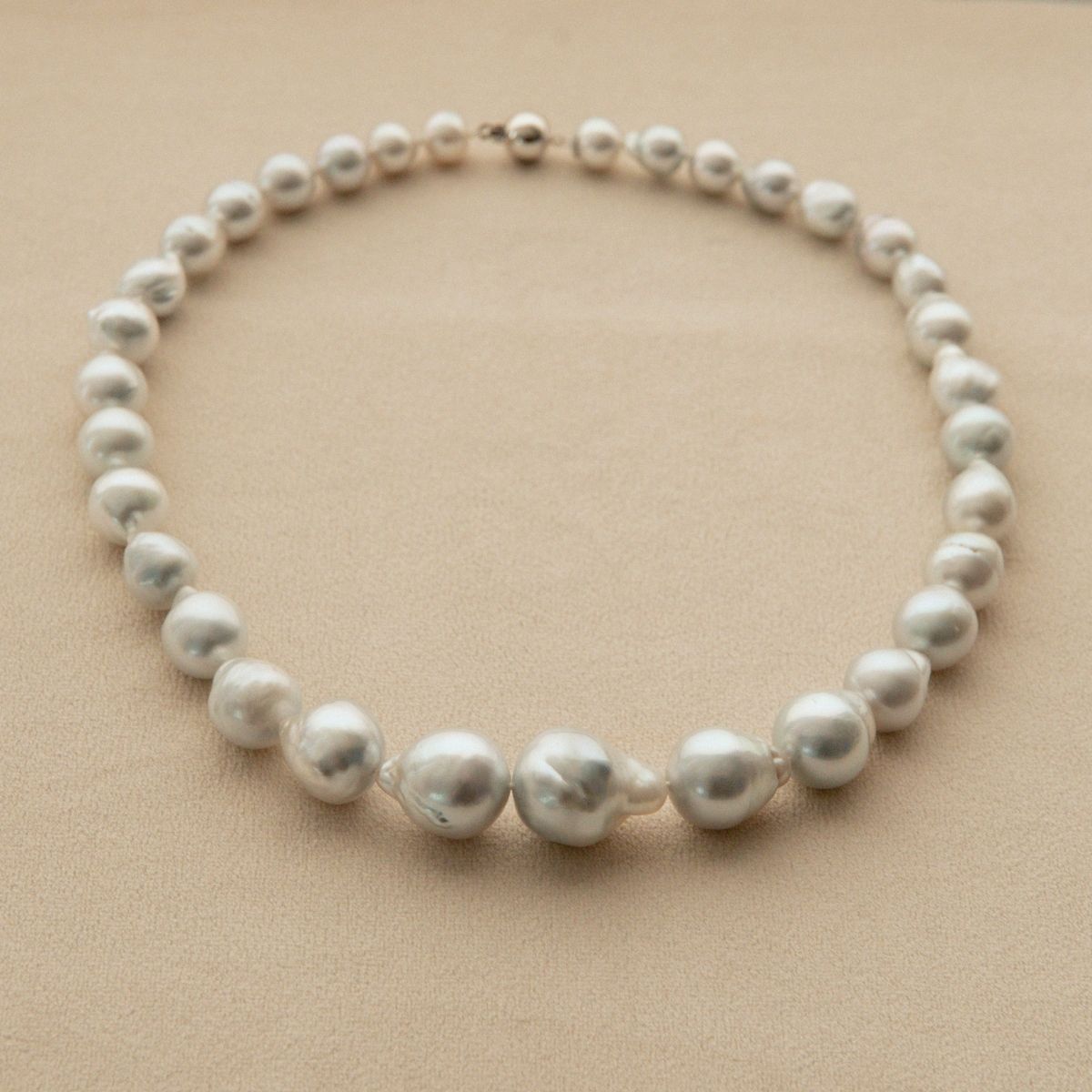 A strand necklace made of irregular baroque Australian South Sea pearls with a small 18ct white gold clasp, displayed on a textured beige background.