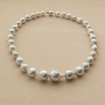 A strand necklace made of irregular baroque Australian South Sea pearls with a small 18ct white gold clasp, displayed on a textured beige background.