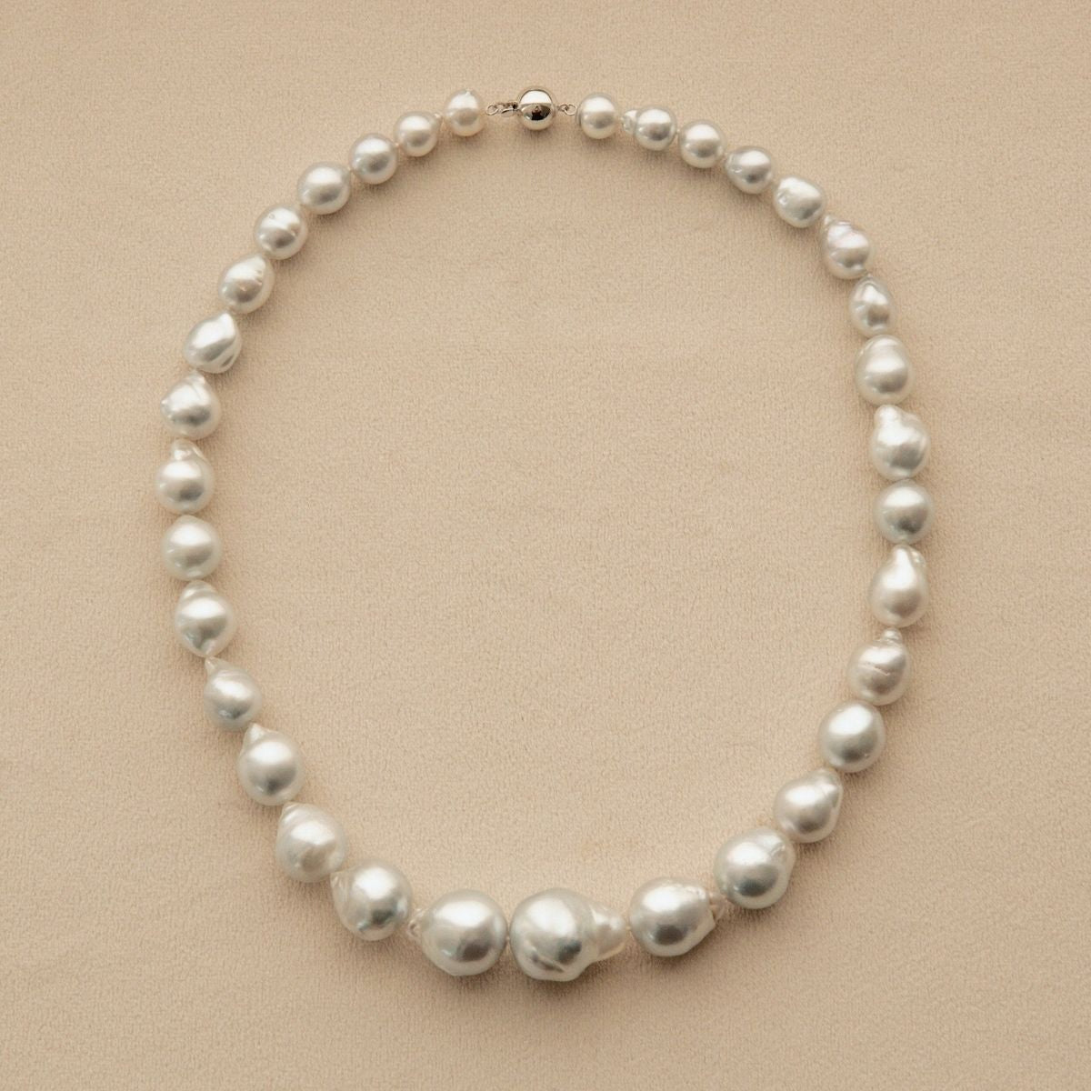 A baroque pearl strand necklace with irregular, Australian South Sea pearls arranged in a circle on a light beige textured background.