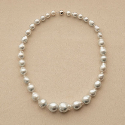 A baroque pearl strand necklace with irregular, Australian South Sea pearls arranged in a circle on a light beige textured background.
