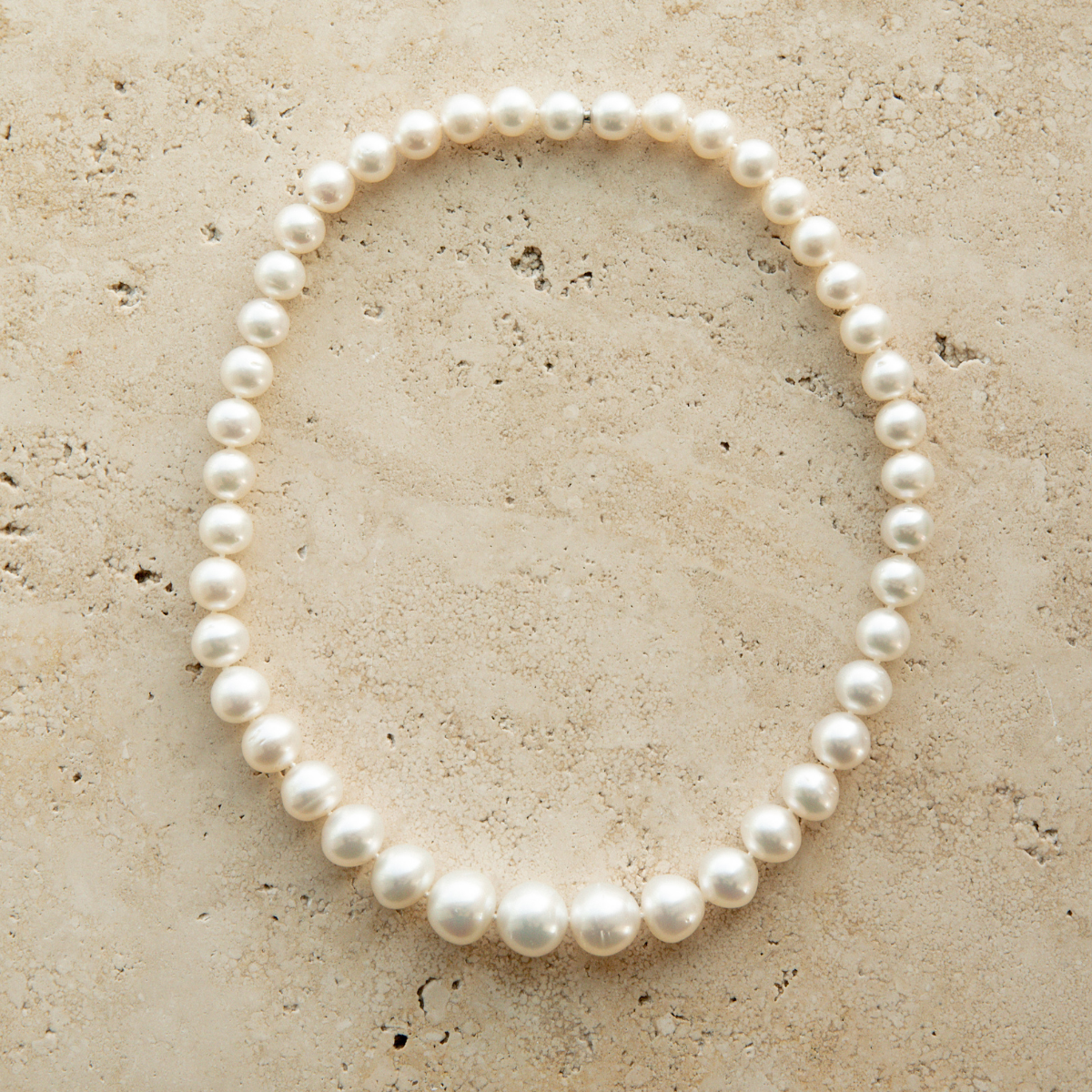 Pearl strand necklace on a textured beige surface