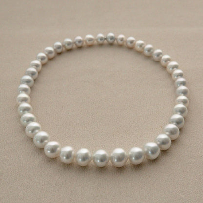 A single strand of round silver Cygnet Bay grown Australian South Sea pearls arranged in a circle on a textured beige surface.