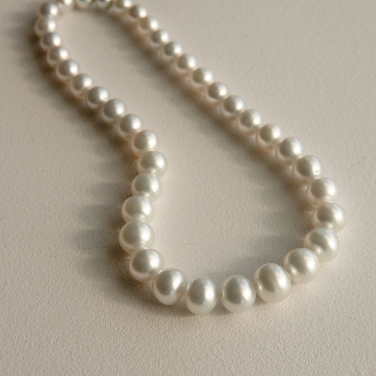 A strand of silver Australian South Sea pearls arranged in a loose loop on a textured beige surface.