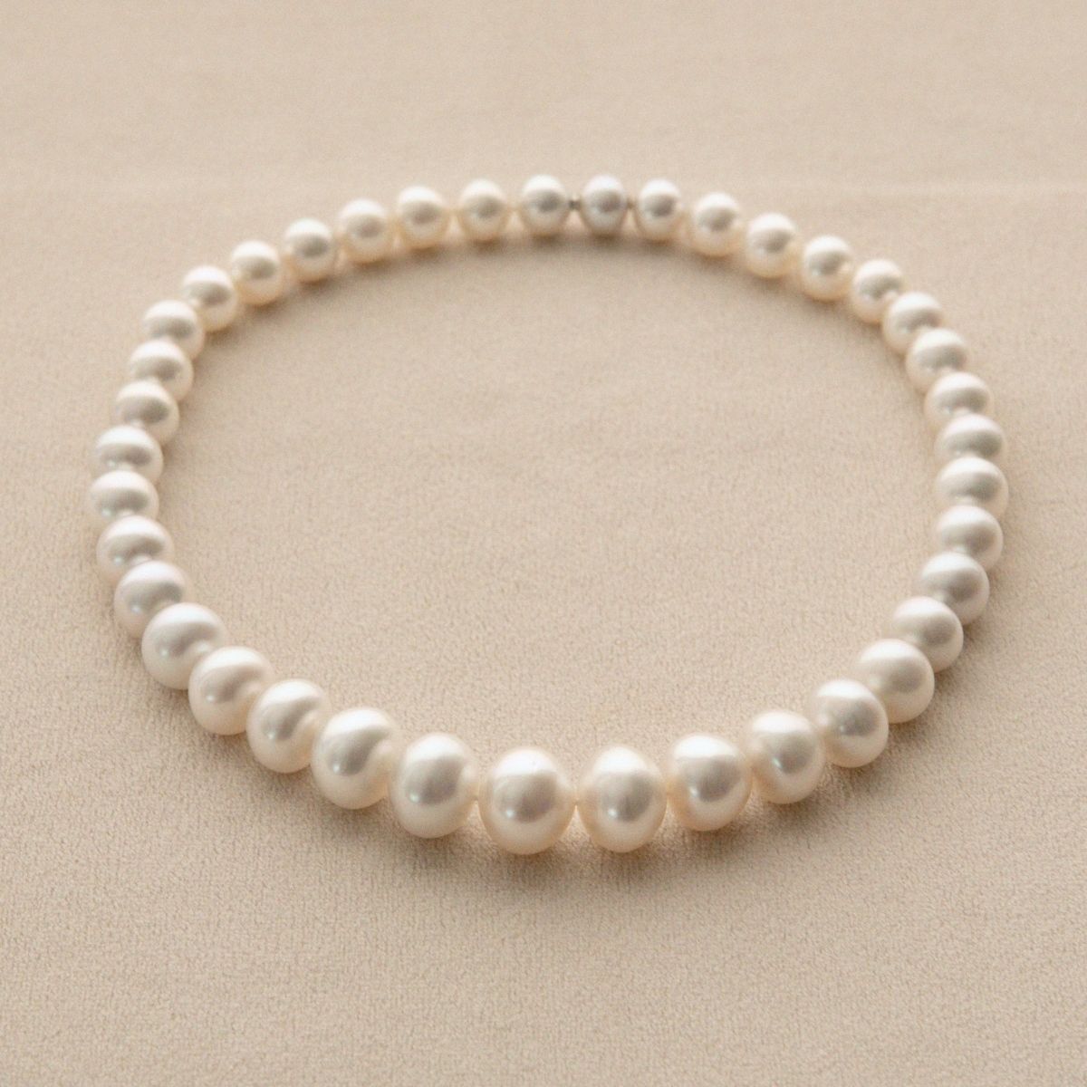 A strand of white Australian South Sea pearls arranged in a circle on a textured beige background.