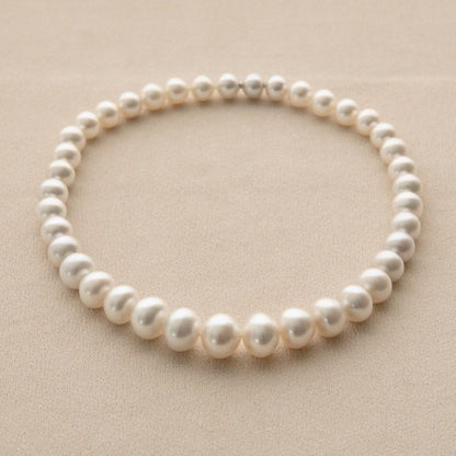 A strand of white Australian South Sea pearls arranged in a circle on a textured beige background.