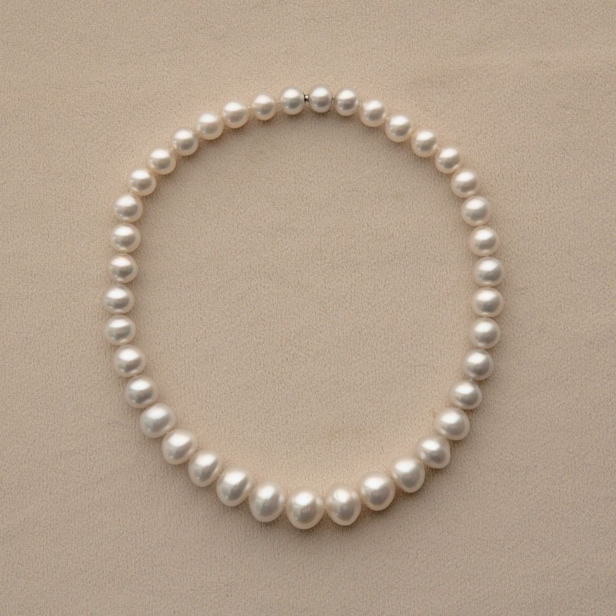 A strand of white Cygnet Bay grown Australian South Sea pearls arranged in a neat circle on a textured beige background.
