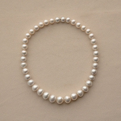A strand of white Cygnet Bay grown Australian South Sea pearls arranged in a neat circle on a textured beige background.