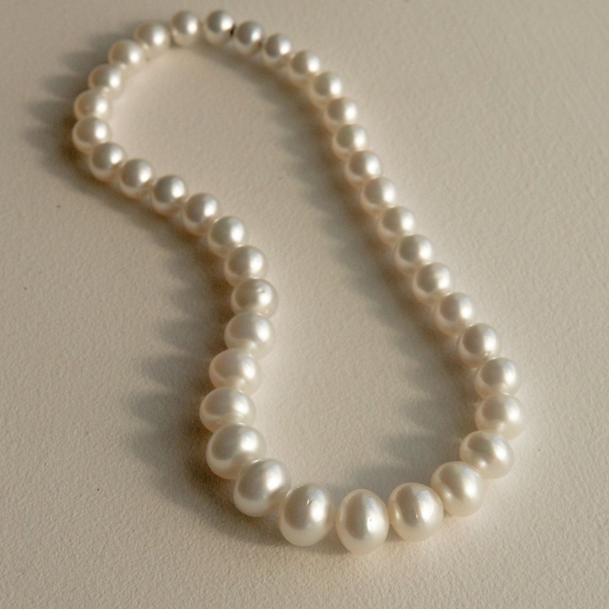 A strand of white Australian-grown South Sea pearls arranged in a loose loop on a light beige textured surface.