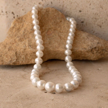 A strand of white Australian South Sea pearls draped over a natural tan rock on a textured stone surface.