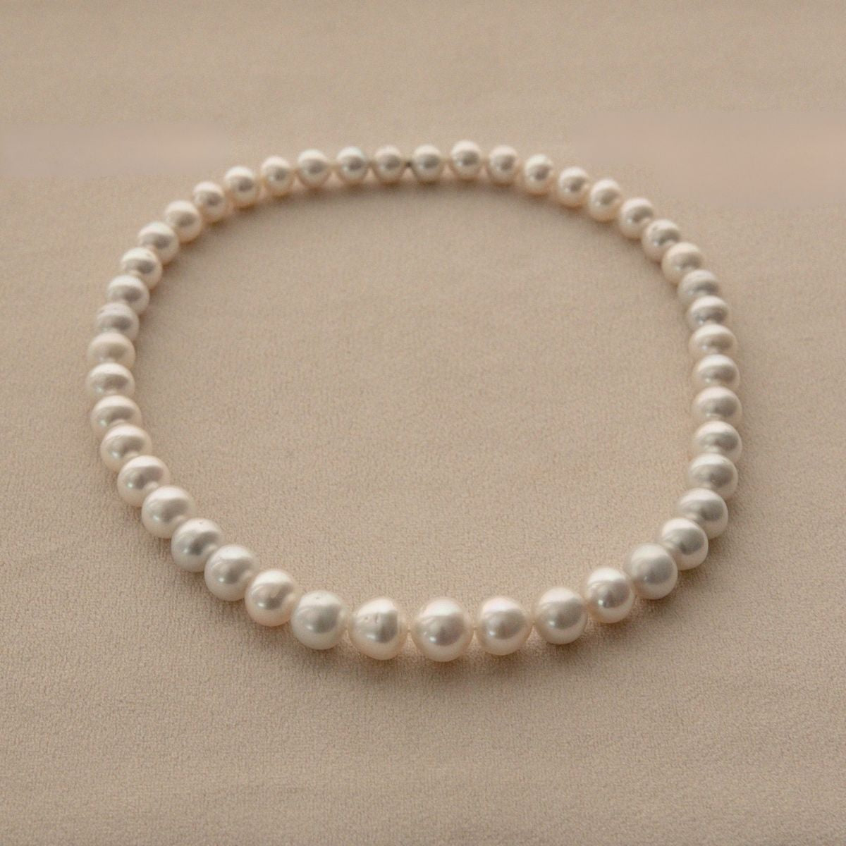 A single strand of white Australian South Sea pearls arranged in a circle on a textured beige background.