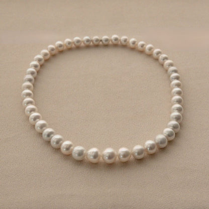 A single strand of white Australian South Sea pearls arranged in a circle on a textured beige background.