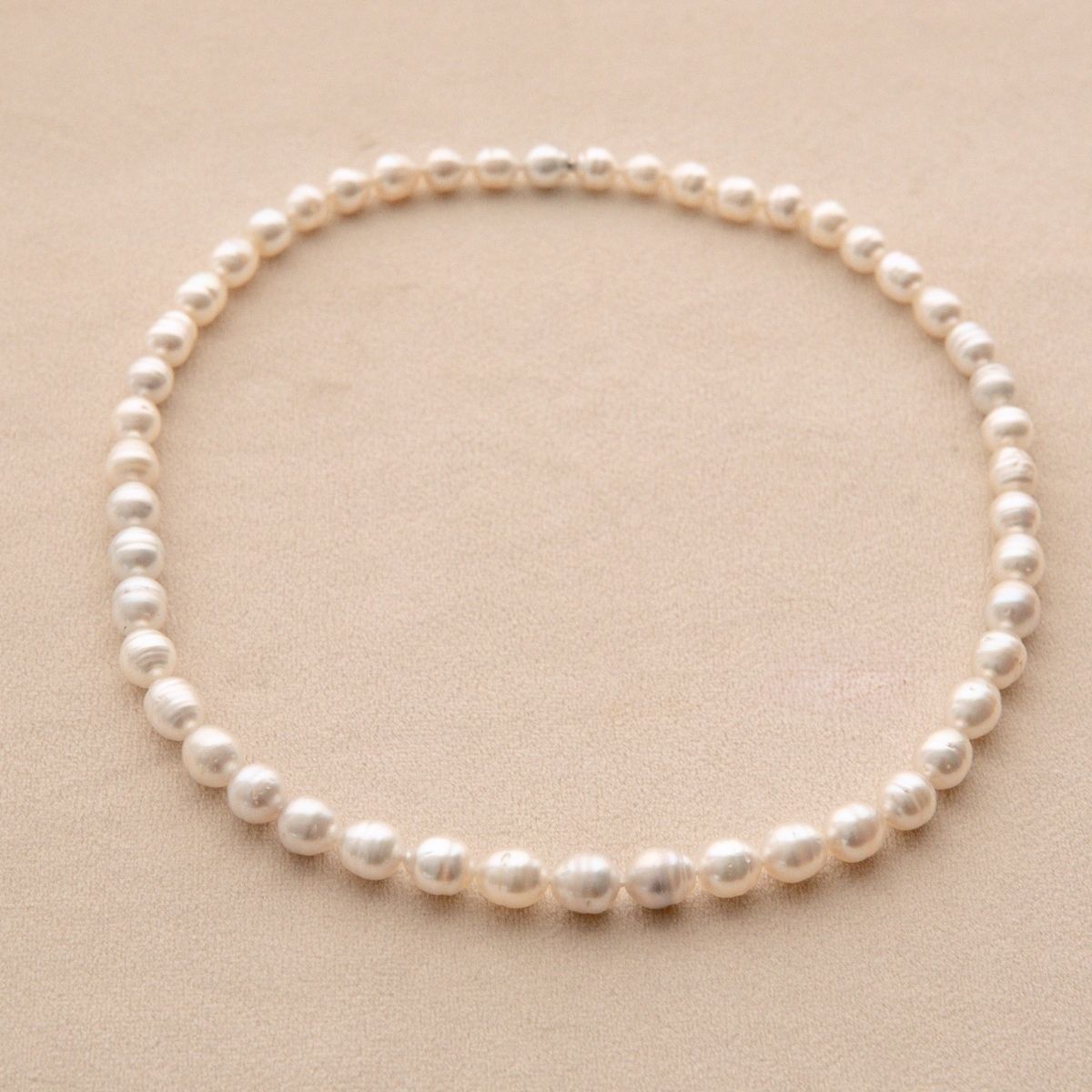A single-strand pearl necklace arranged in a circle on a textured beige background.