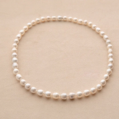 A single-strand pearl necklace arranged in a circle on a textured beige background.
