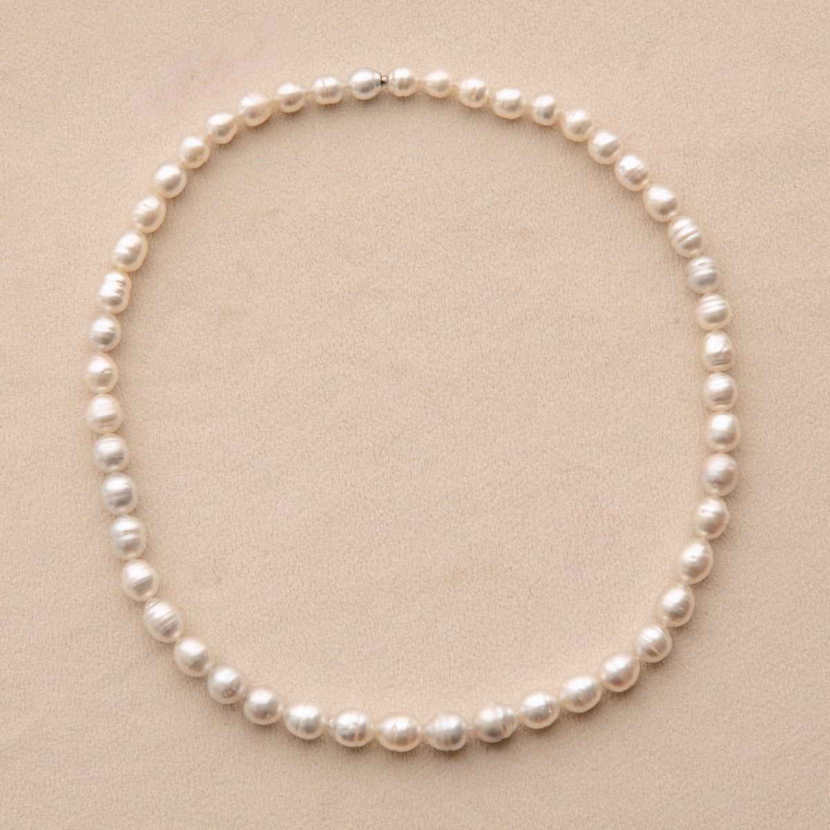 A single strand of irregular Australian South Sea pearls arranged in a circle on a light beige textured background.