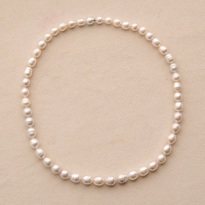 A single strand of irregular Australian South Sea pearls arranged in a circle on a light beige textured background.
